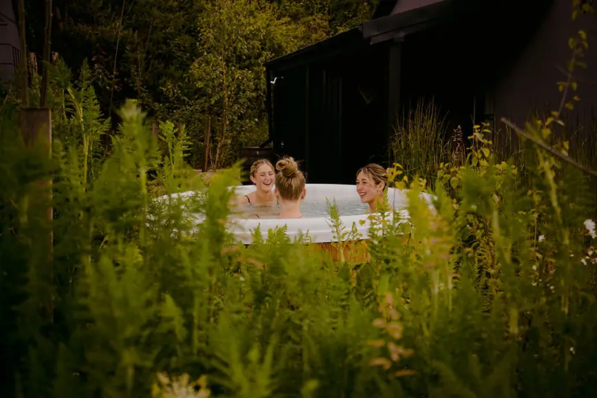 Women laughing in an outdoor hot tub surrounded by ferns