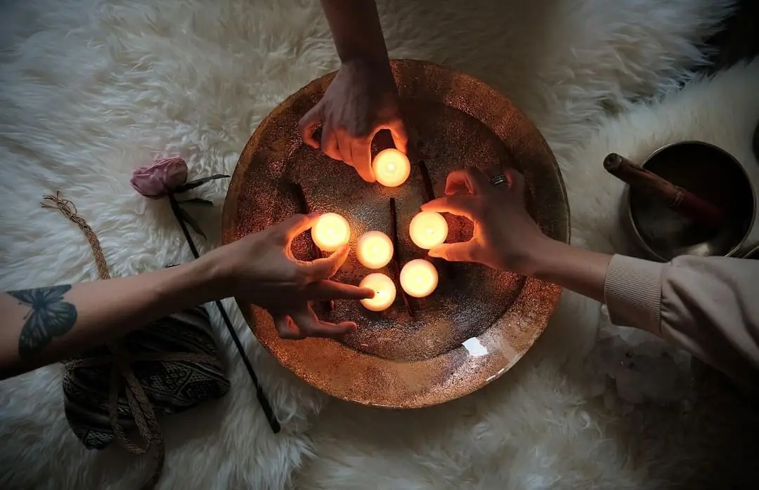 Three pairs of hands holding candles over a copper bowl